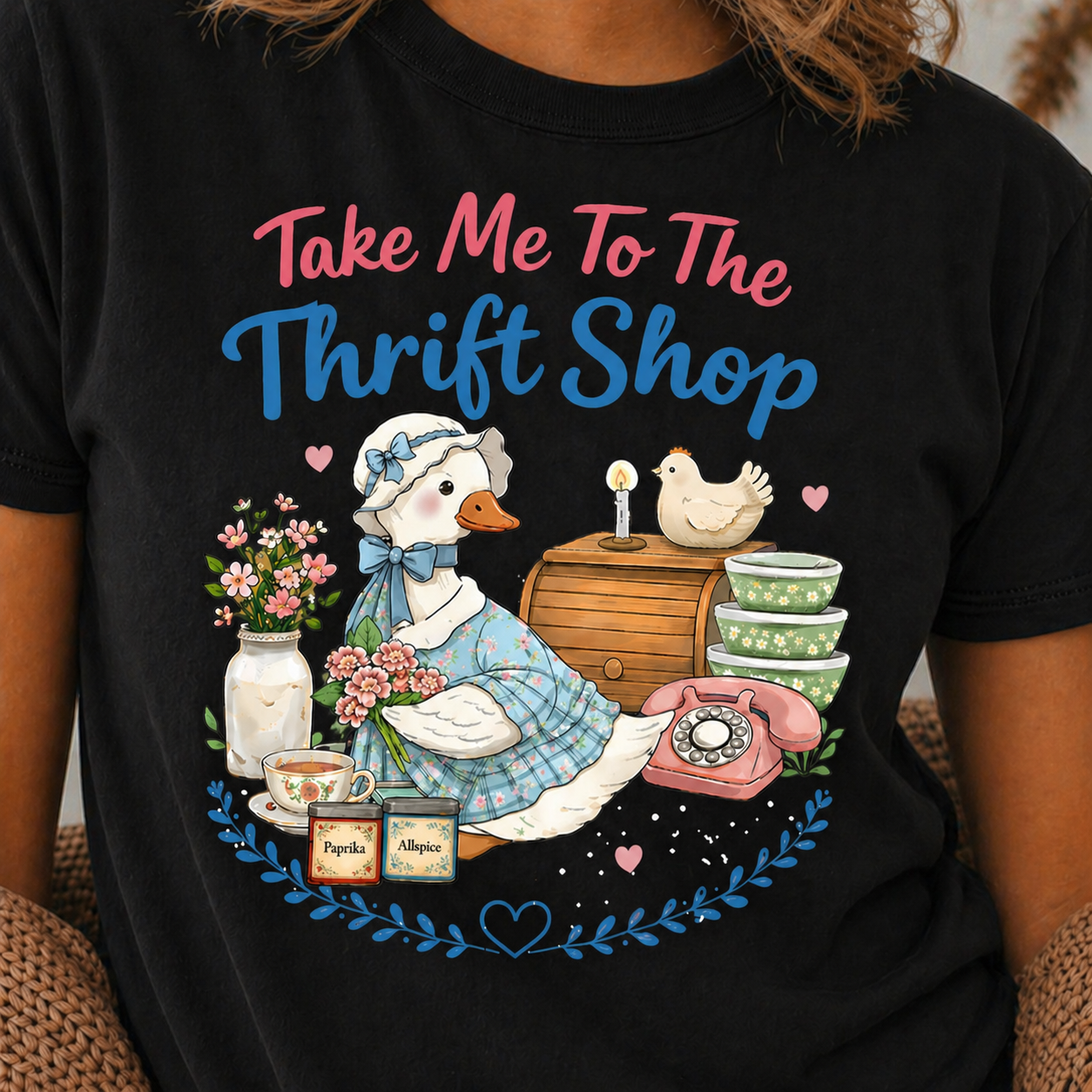 Black t-shirt with a graphic of a goose, flowers, and text 'Take Me To The Thrift Shop' worn by a person.