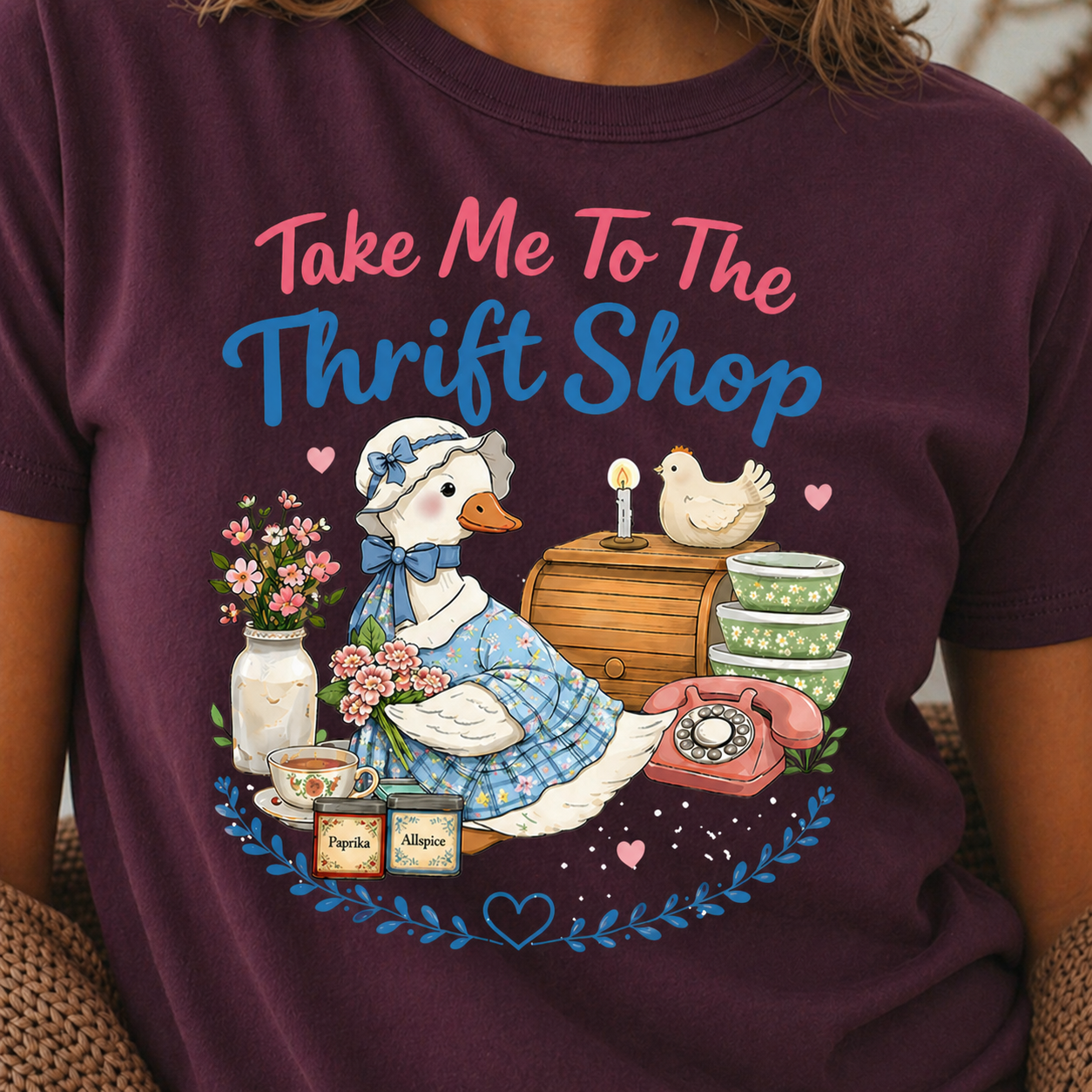Person wearing a maroon t-shirt with a graphic of a duck, flowers, and text 'Take Me To The Thrift Shop'.