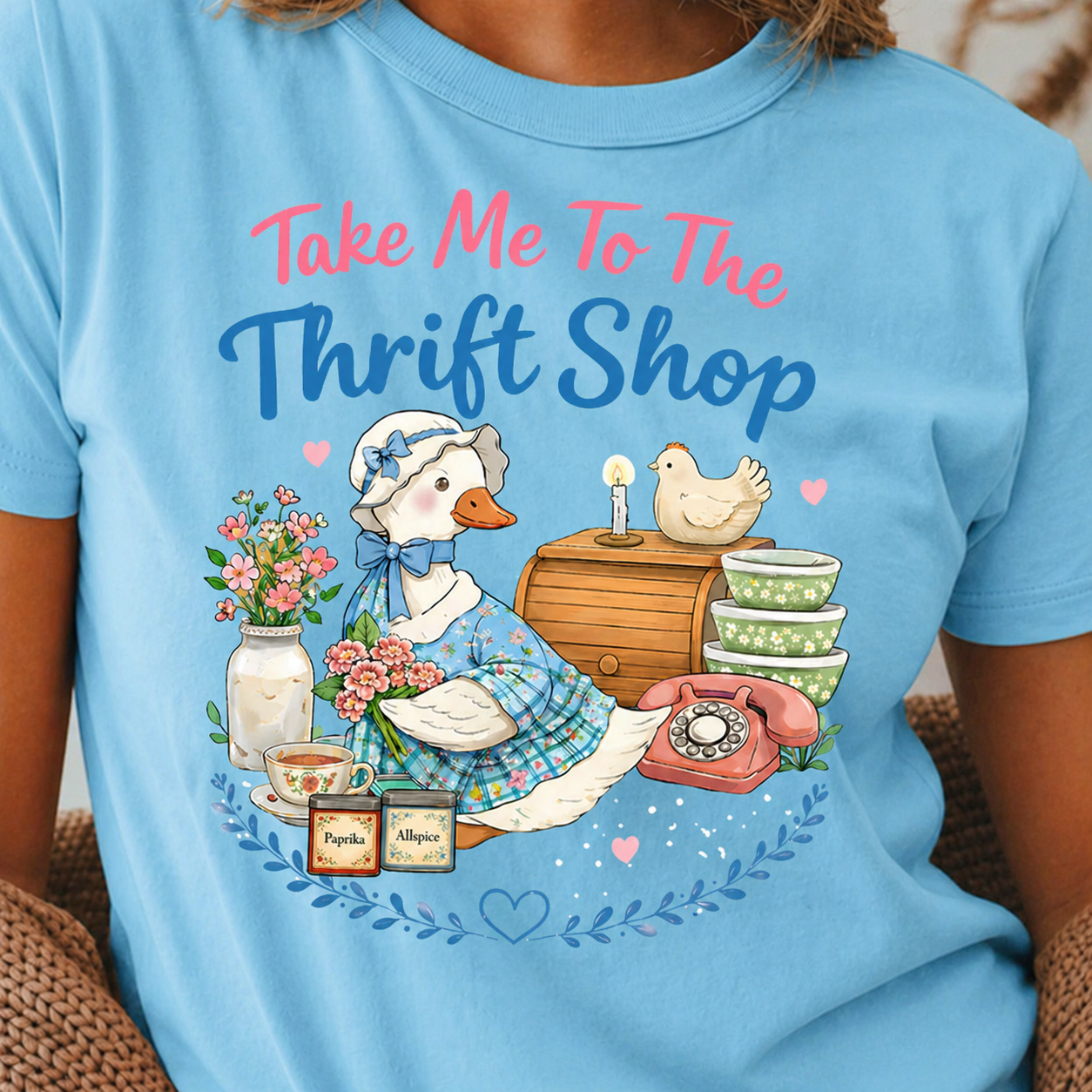 Sky blue t-shirt with a graphic of ducks, flowers, and text 'Take Me To The Thrift Shop' on a person wearing it.