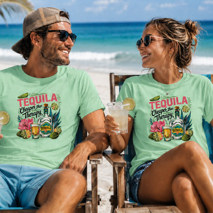 A man and a woman sitting on beach chairs at the ocean, both wearing matching light green graphic T-shirts with a colorful 'Tequila Cheers in Tampa, FL' design. The man wears a tan cap and sunglasses, and the woman wears sunglasses, with a tropical beach background.