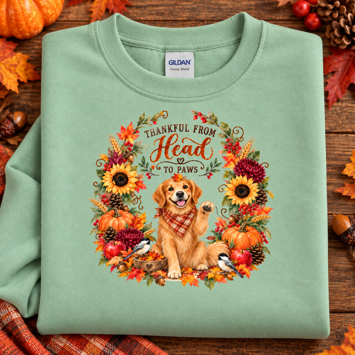 A folded mint green Gildan Heavy Weight sweatshirt with a detailed autumn-themed graphic of a golden retriever surrounded by a fall wreath, displayed on a rustic wooden background with seasonal props.