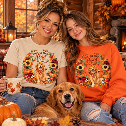 Two women and a golden retriever dog sit together in a cozy fall-themed room, wearing matching graphic t-shirt and sweatshirt designs. The beige t-shirt and orange sweatshirt both feature a dog wearing a bandana surrounded by autumn leaves and sunflowers, with the text 'TANKERY FROM Head Go To Paws'.