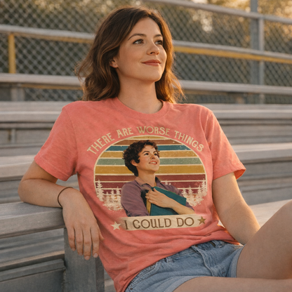 Woman wearing a t-shirt with a graphic and text, sitting on bleachers.