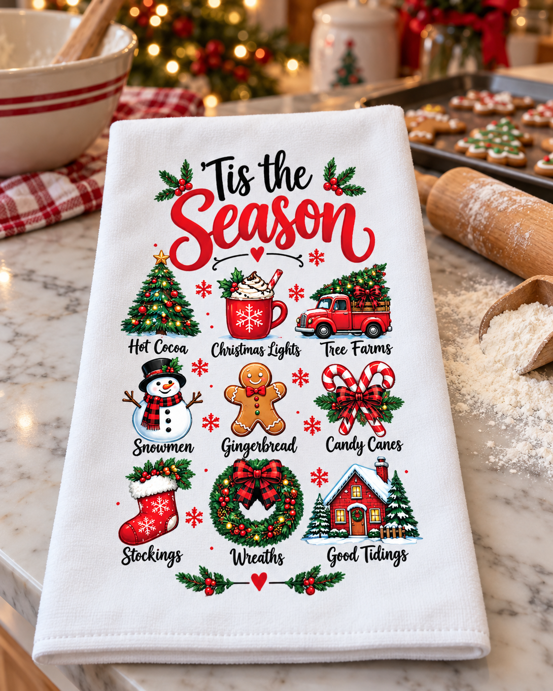 A white kitchen towel with a festive Christmas graphic print, displayed on a marble countertop with blurred holiday baking props in the background.