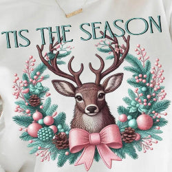 Christmas sweatshirt featuring a reindeer framed by a pink and teal faux-embroidered wreath with festive accents and a pink bow.