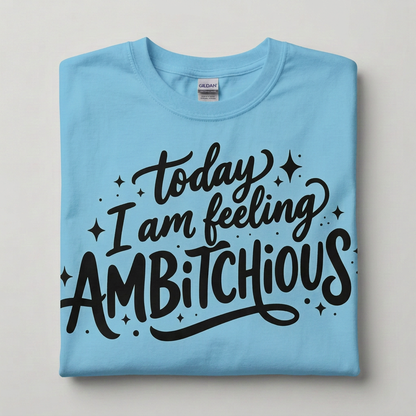A folded sky blue Gildan t-shirt with a black hand-lettered graphic that reads 'today I am feeling AMBITCHIOUS' surrounded by small star and dot accents, displayed on a neutral light gray background.