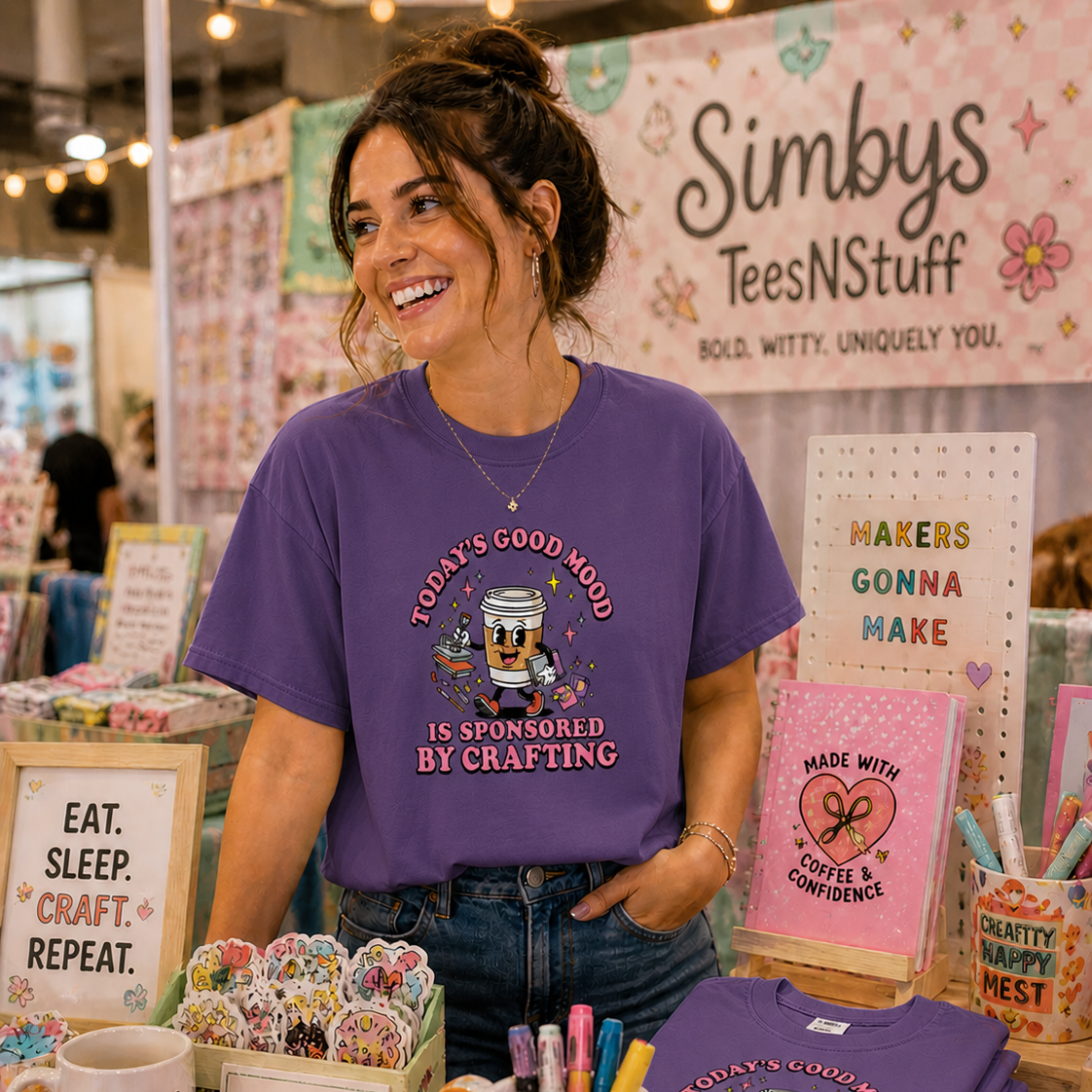 Woman wearing a purple t-shirt with a graphic design at a craft fair booth.