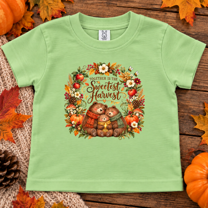 A keylime green short-sleeve baby t-shirt with a 'Together is the Sweetest Harvest' autumn graphic, displayed flat on a rustic wooden background with pumpkins and fall leaves.