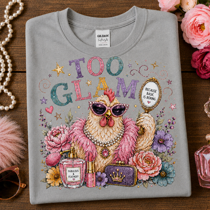 A folded sport gray t-shirt with a colorful graphic print of a fashionable chicken wearing sunglasses and a pearl necklace, surrounded by flowers, perfume bottles, and a mirror that reads 'BEIGE BLACK OR BURNING'. The shirt is displayed on a wooden surface with decorative props including pink roses, a pearl necklace, and sunglasses.