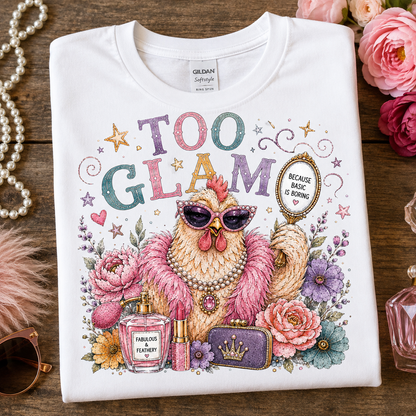 A folded white Gildan Softee T-shirt is displayed on a rustic wooden surface surrounded by pink roses, a pearl necklace, a pink feather boa, and perfume bottles. The shirt features a colorful graphic of a chicken wearing sunglasses and a pink feather boa, surrounded by flowers and cosmetics, with the text 'TOO GLAM' and a badge reading 'BECAUSE BRASH IS BORN'.