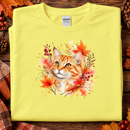 A cornsilk yellow colored t-shirt with Watercolor-style graphic design of an orange tabby cat surrounded by autumn leaves, berries, and warm paint splashes on a white background.