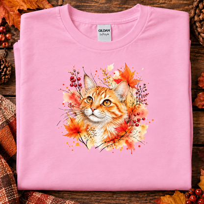 A fan candy pink colored t-shirt with Watercolor-style graphic design of an orange tabby cat surrounded by autumn leaves, berries, and warm paint splashes on a white background.