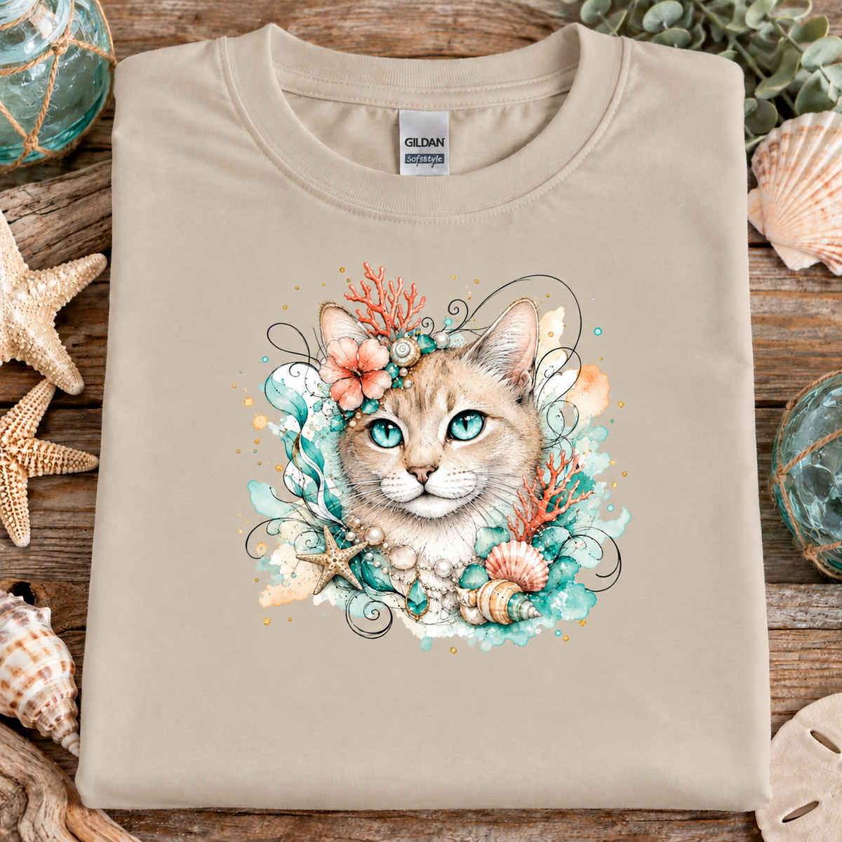 A sand colored t-shirt with a tan tabby cat surrounded by seashells