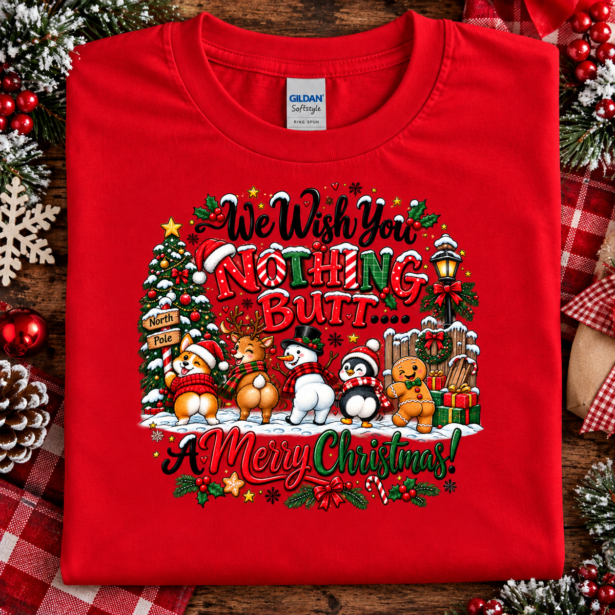A folded red t-shirt with a colorful Christmas graphic on the front, displayed on a rustic wooden background with holiday decorations like pinecones, berries, and a plaid ribbon. The shirt features the text 'We Wish You NOTHING BUT.