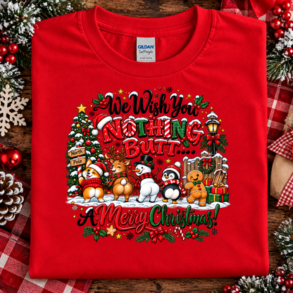 A folded red t-shirt with a colorful Christmas graphic on the front, displayed on a rustic wooden background with holiday decorations like pinecones, berries, and a plaid ribbon. The shirt features the text 'We Wish You NOTHING BUT.