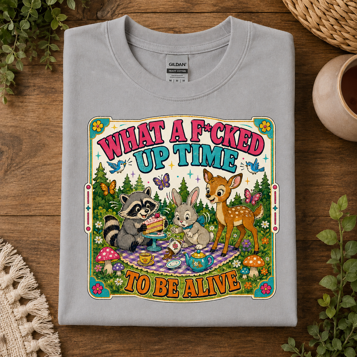A spport gray Gildan crewneck t-shirt with a colorful graphic print of a raccoon, rabbit, and deer having an Easter picnic. The text reads 'WHAT A F*CKED UP TIME TO BE ALIVE'.