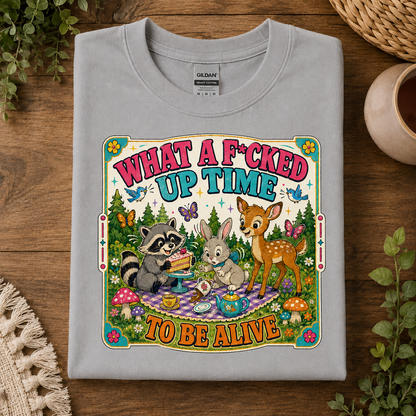 A spport gray Gildan crewneck t-shirt with a colorful graphic print of a raccoon, rabbit, and deer having an Easter picnic. The text reads 'WHAT A F*CKED UP TIME TO BE ALIVE'.