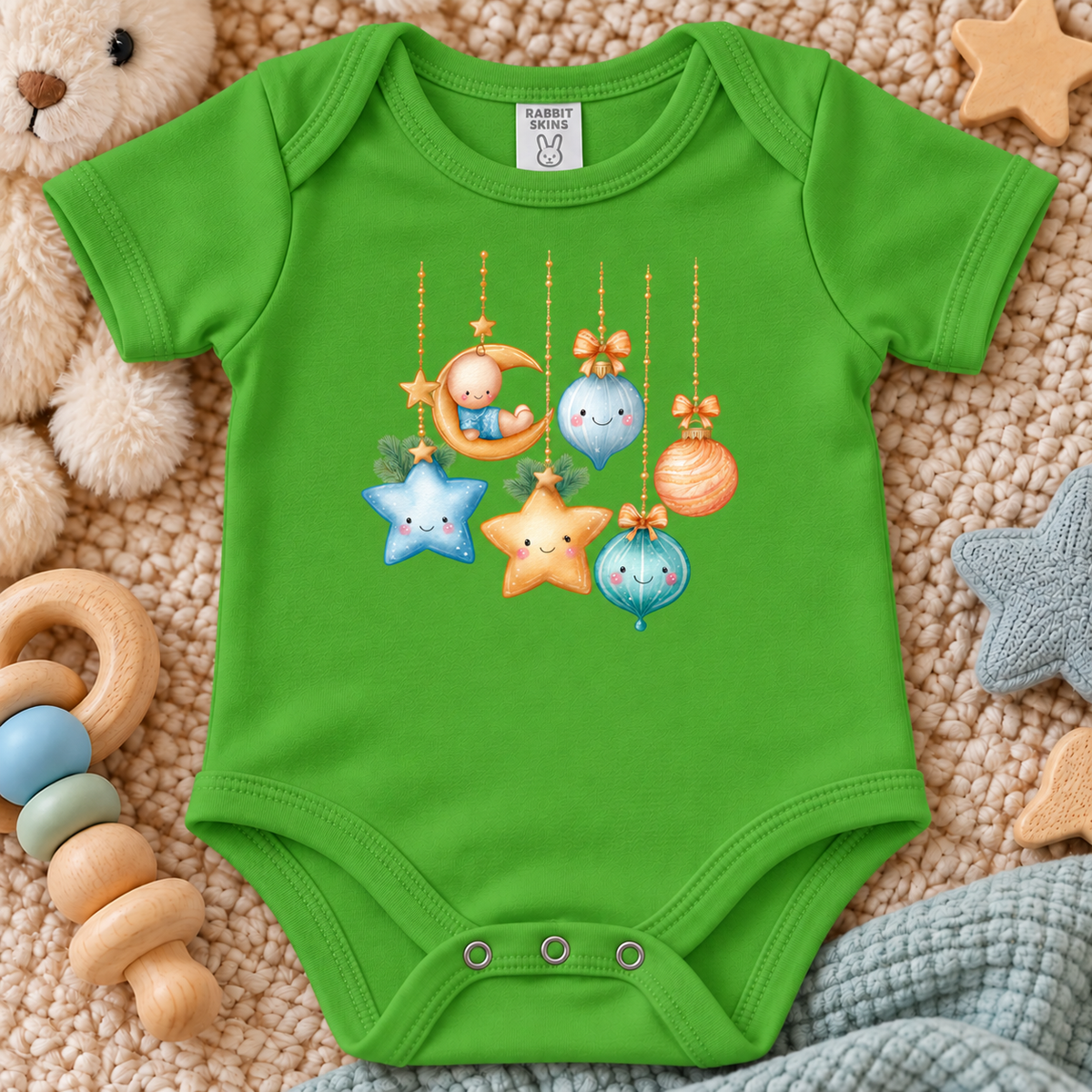 A apple green baby bodysuit with a cute cartoon Christmas ornament graphic, laid flat on a soft beige blanket with baby toys around it.