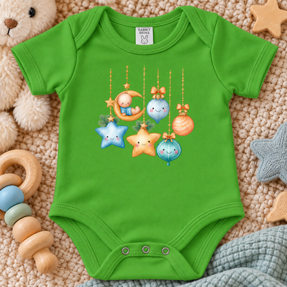 A apple green baby bodysuit with a cute cartoon Christmas ornament graphic, laid flat on a soft beige blanket with baby toys around it.