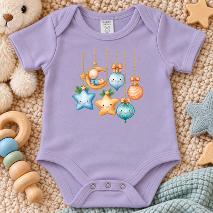 A lavender baby bodysuit with a colorful graphic of cute hanging ornaments, styled in a cozy flat-lay with toys and a teddy bear.
