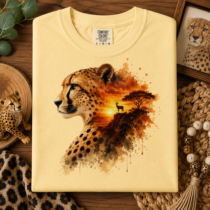 A folded butter colored t-shirt with a detailed cheetah graphic print, styled on a rustic wooden background with safari-themed props.
