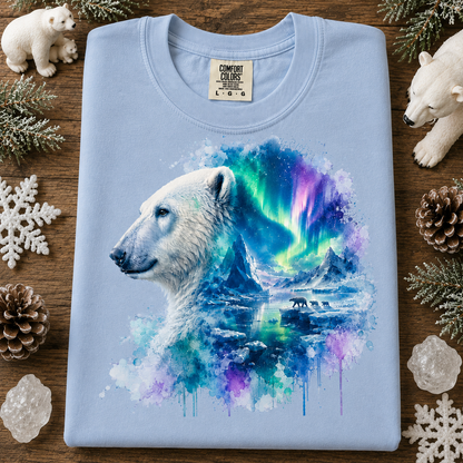 A folded light blue(hydranges) t-shirt with a detailed graphic print of a polar bear in profile, blending into an arctic landscape with aurora borealis. The shirt is displayed on a rustic wooden background surrounded by decorative snowflakes, pinecones, and polar bear figurines.