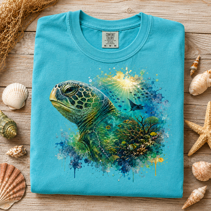 A folded lagoon blue t-shirt with a colorful sea turtle and coral graphic, styled on a wooden surface with seashells and netting.