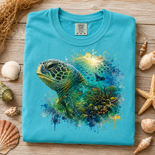 A folded lagoon blue t-shirt with a colorful sea turtle and coral graphic, styled on a wooden surface with seashells and netting.
