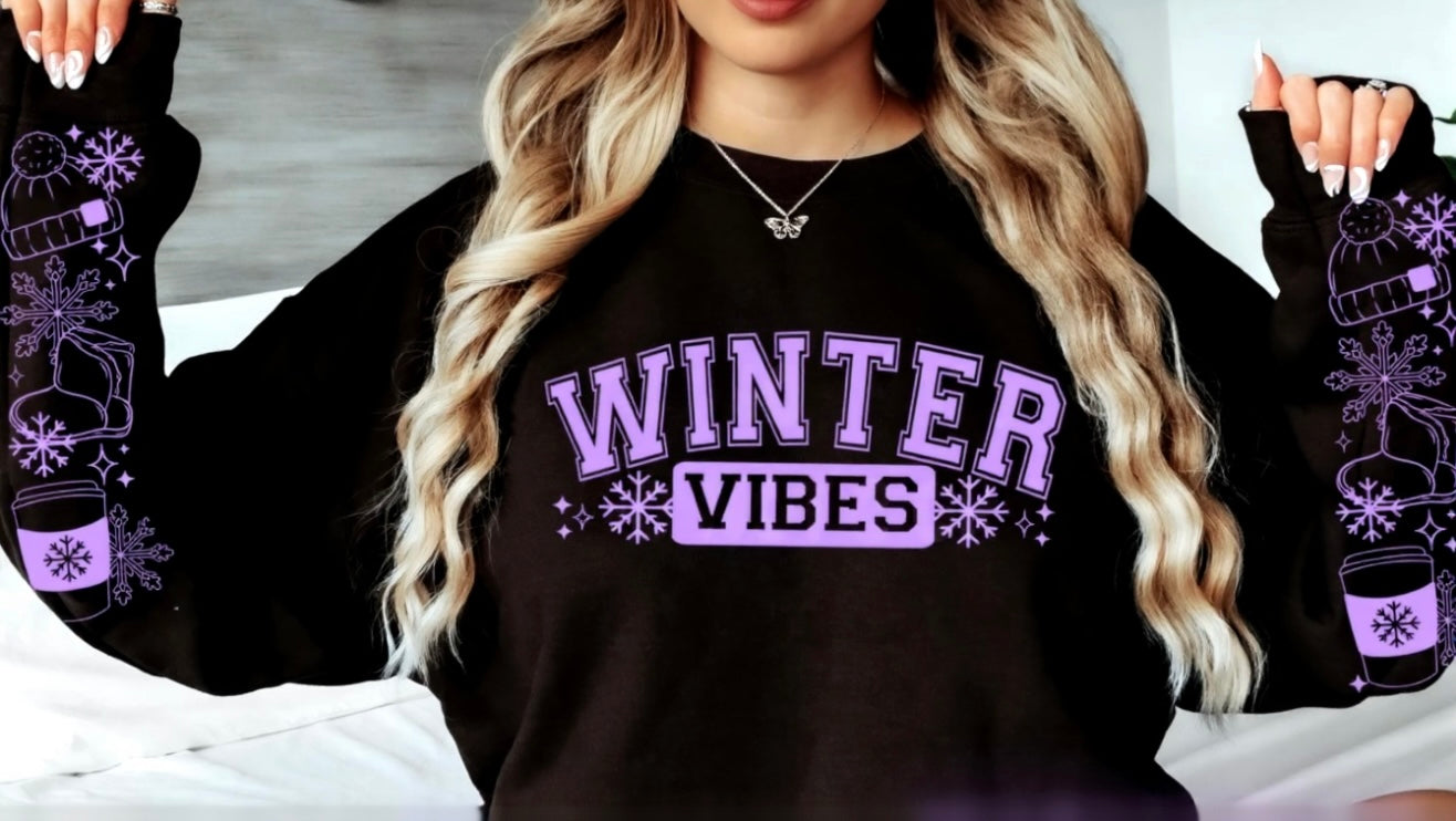 Black sweatshirt with 'Winter Vibes' text and winter-themed graphics worn by a person.