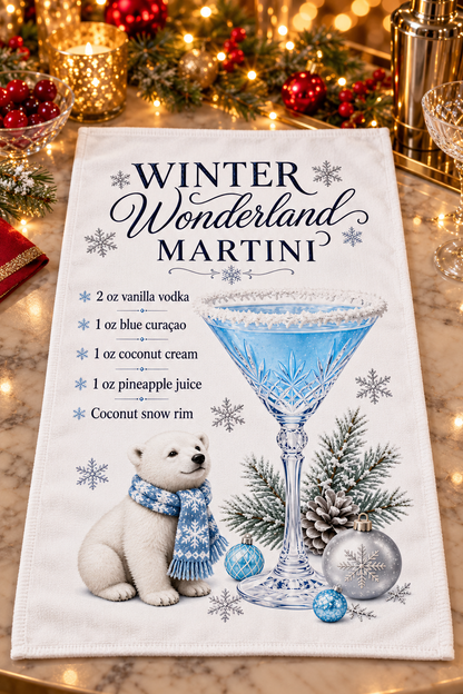A white kitchen towel featuring a festive 'Winter Wonderland Martini' design, styled on a marble countertop with holiday lights and decorations in the background.