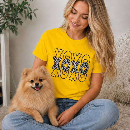 Woman wearing a yellow t-shirt with 'XOXO' design sitting with a small dog indoors.