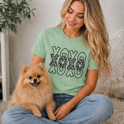 Woman wearing a mint green t-shirt with 'XOXO' design sitting with a small dog indoors.