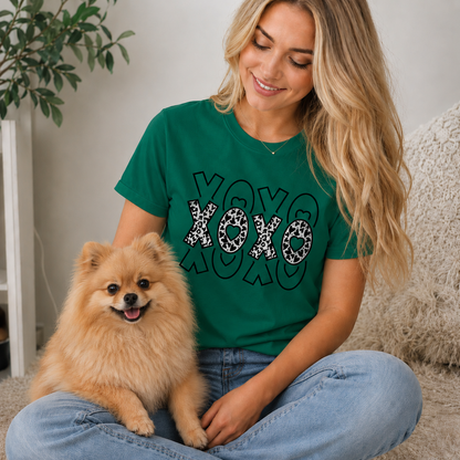 Woman wearing a sapphire t-shirt with 'XOXO' design sitting with a small dog indoors.