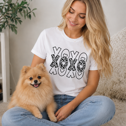 Woman wearing a white t-shirt with 'XOXO' design sitting with a small dog indoors.