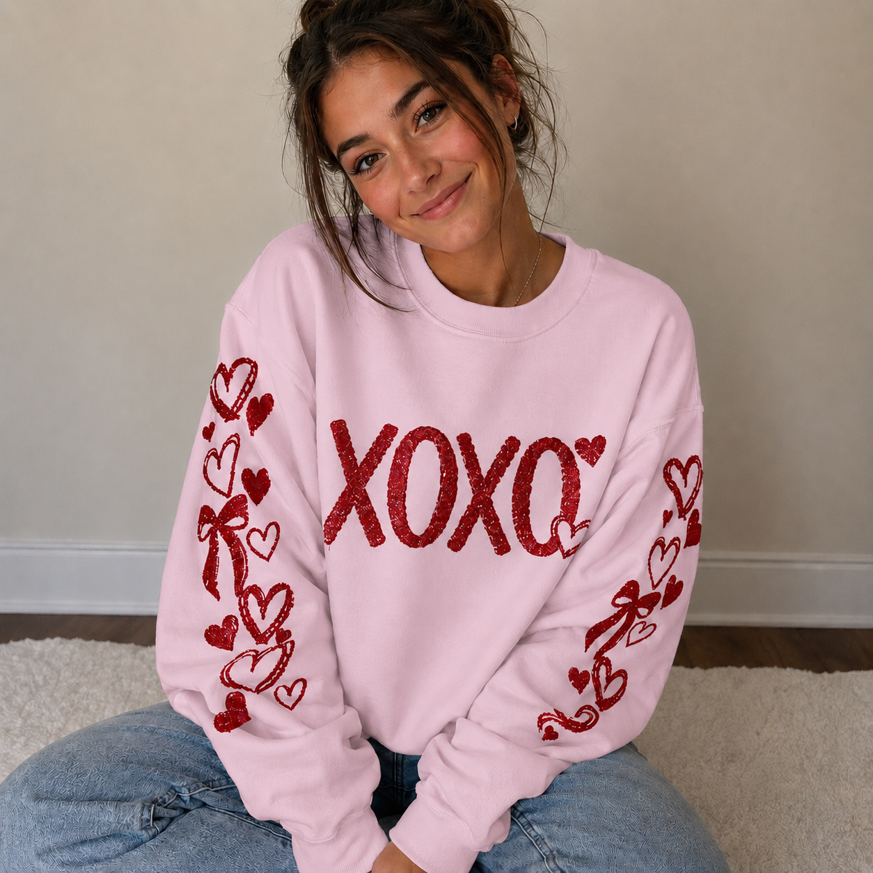 Person wearing a pink sweatshirt with red heart and bow designs, sitting on a carpeted floor.