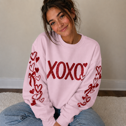 Person wearing a pink sweatshirt with red heart and bow designs, sitting on a carpeted floor.