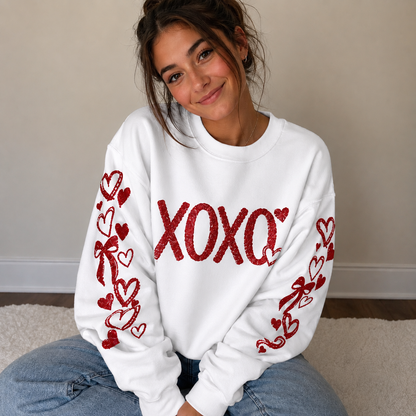 Person wearing a white sweatshirt with red 'XOXO' and heart designs, sitting on a carpeted floor.