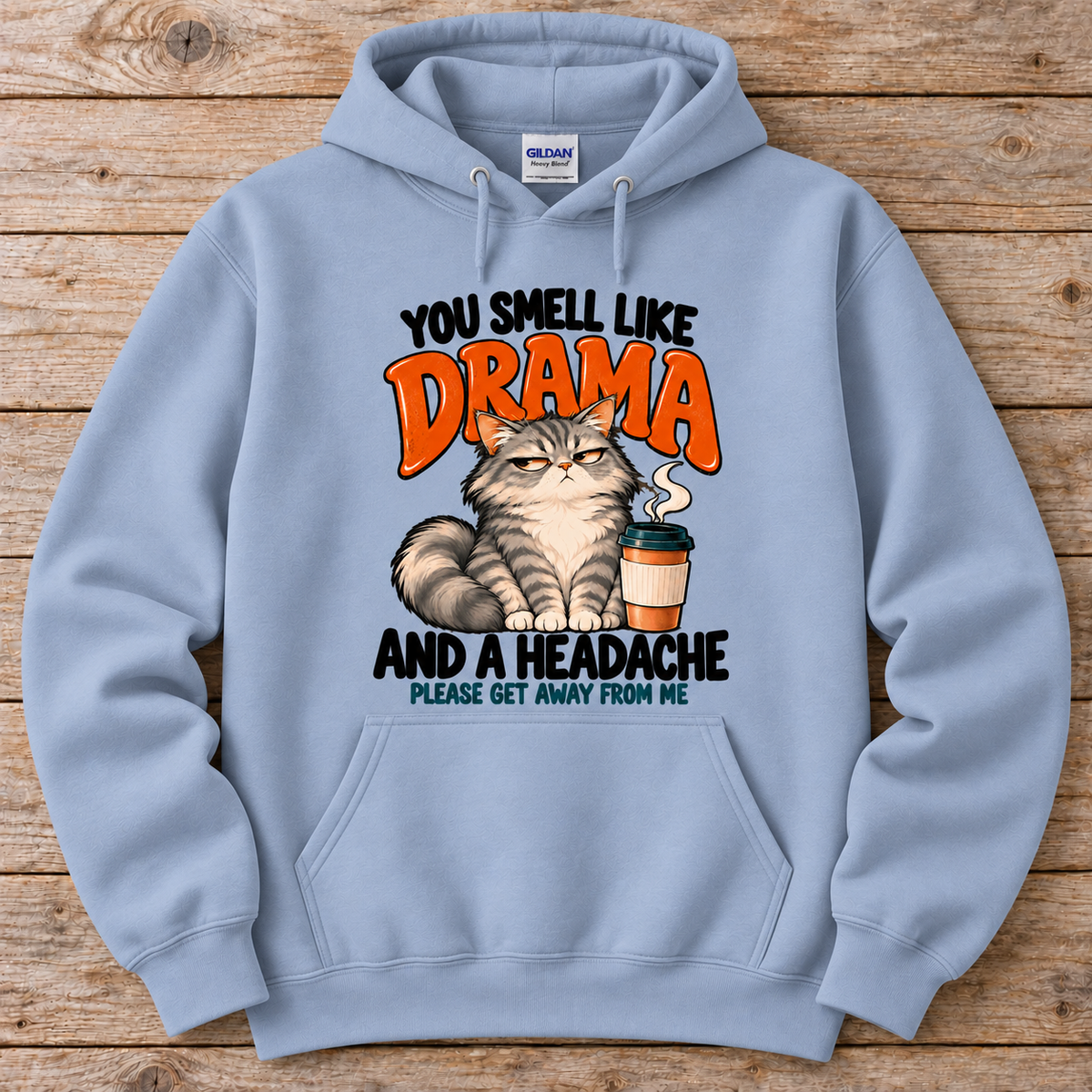 A light blue crewneck hoodie featuring a humorous graphic print of a grumpy cat next to a coffee cup, with the text 'YOU SMELL LIKE DRAMA AND A HEADACHE PLEASE GET AWAY FROM ME'. 