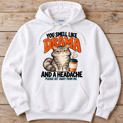 A white Gildan hoodie laid flat on a rustic wooden background, featuring a humorous graphic print of a grumpy cat next to a coffee cup with the text 'YOU SMELL LIKE DRAMA AND A HEADACHE PLEASE GET AWAY FROM ME'.