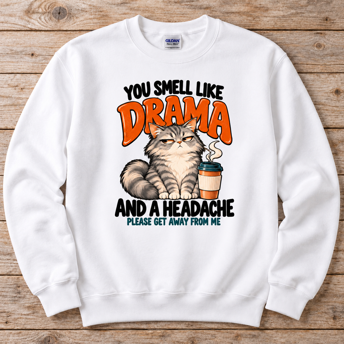 A white crewneck sweatshirt featuring a humorous graphic print of a grumpy cat next to a coffee cup, with the text 'YOU SMELL LIKE DRAMA AND A HEADACHE PLEASE GET AWAY FROM ME'. 
