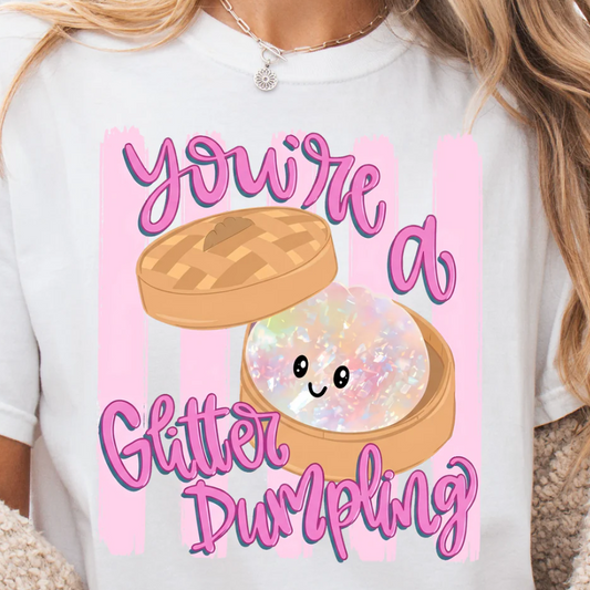 Cute You’re A Glitter Dumpling graphic on a white t-shirt featuring a kawaii pastel dumpling character with glitter-inspired artwork and pink lettering.
