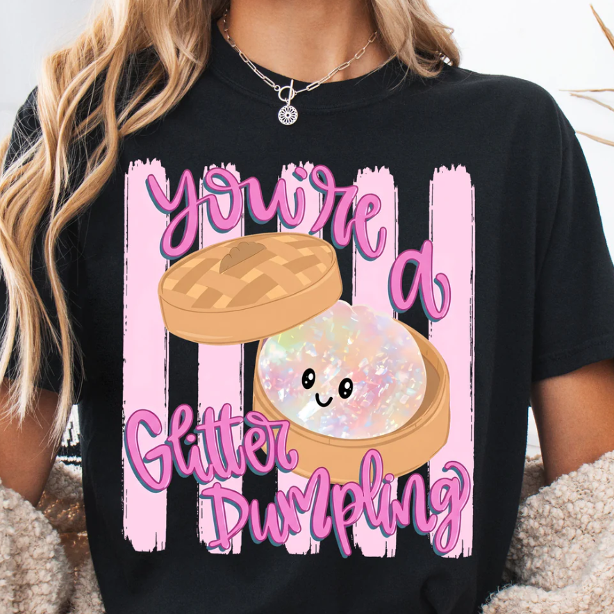 Cute You’re A Glitter Dumpling graphic on a black t-shirt featuring a kawaii pastel dumpling character with glitter-inspired artwork and pink lettering.