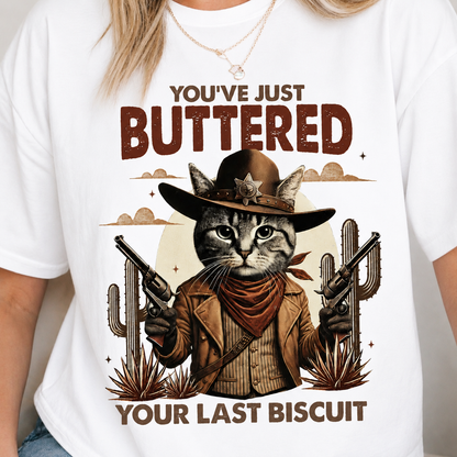 White t-shirt with a graphic of a cat in a cowboy outfit and text You've buttered your last biscuit 