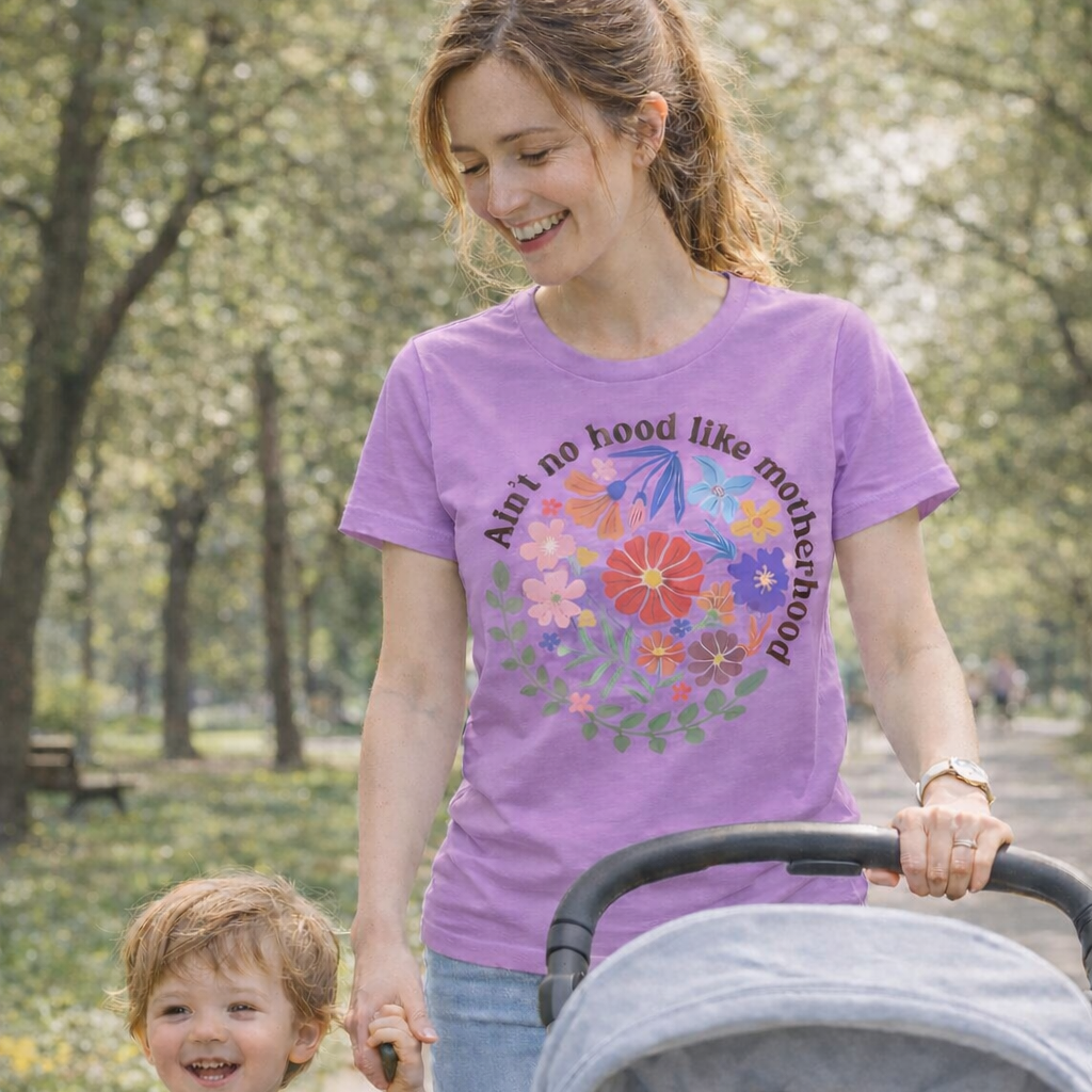 Woman walking with a child and stroller in a park, wearing a purple t-shirt with a colorful design.