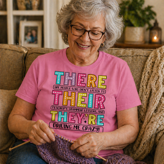 Woman wearing a pink t-shirt with colorful text, sitting on a couch and knitting.