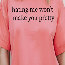 Close-up of a pink T-shirt with the text 'hating me won't make you pretty' printed in bold black letters.