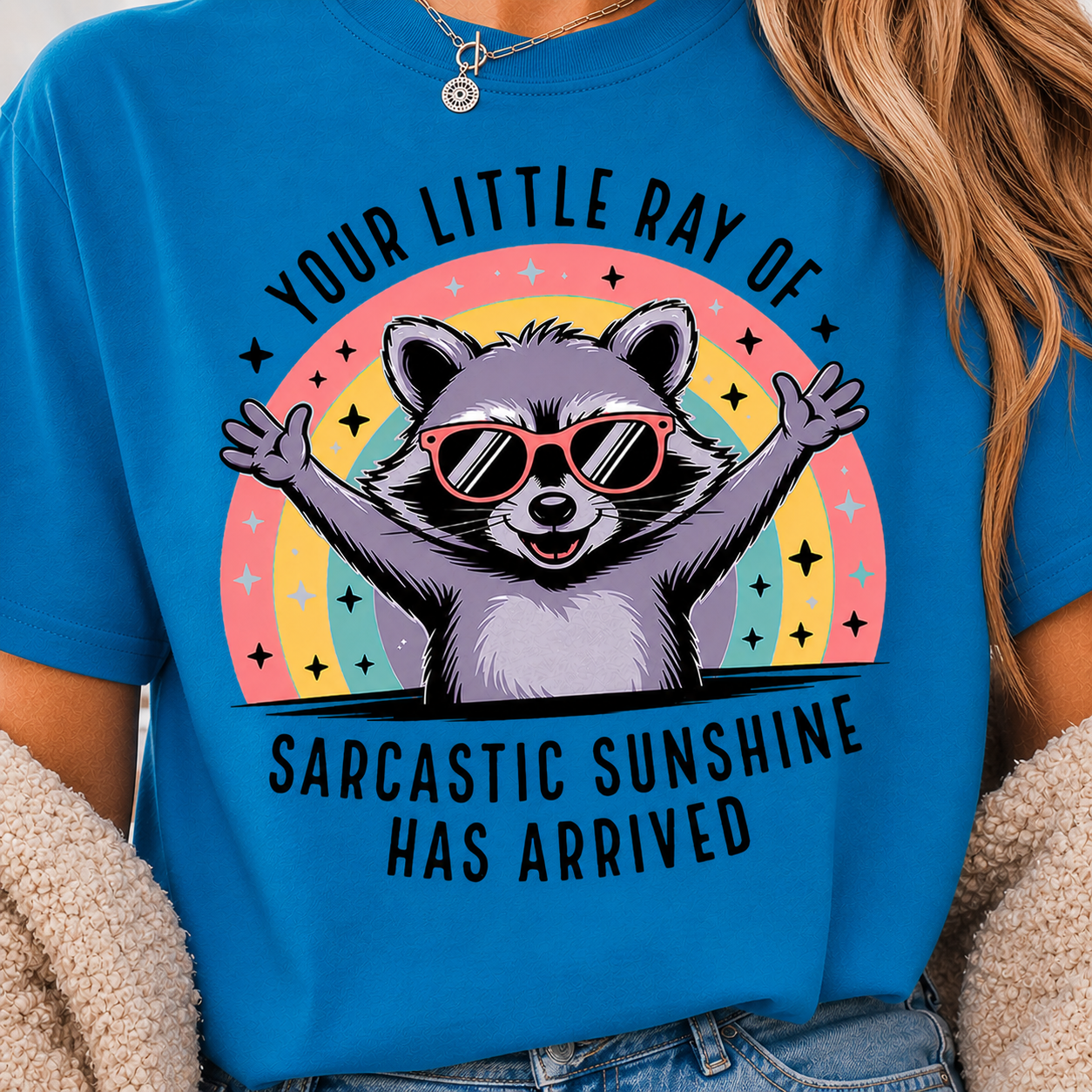 Sarcastic raccoon with arms wide open wearing sunglasses in front of a rainbow design on a Sapphire Comfort Colors Shirt